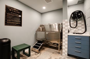 A blackboard menu is on the wall of a room with a stainless steel sink and a green stool